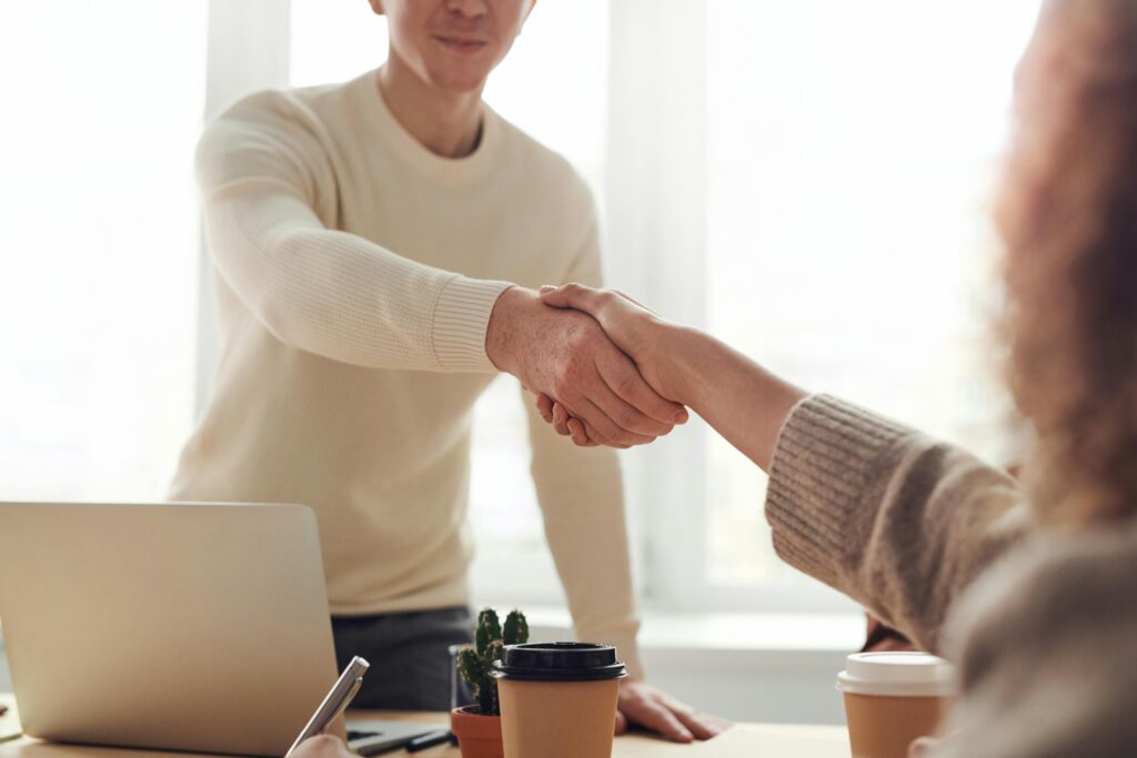 A man standing behind a desk and laptop shakes a woman’s hand