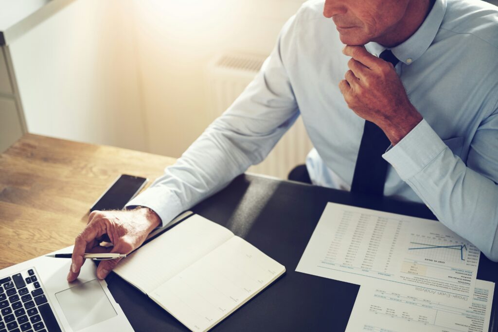 Man in a shirt and tie reviewing business documents, ready to dispute a business credit report, at his desk.