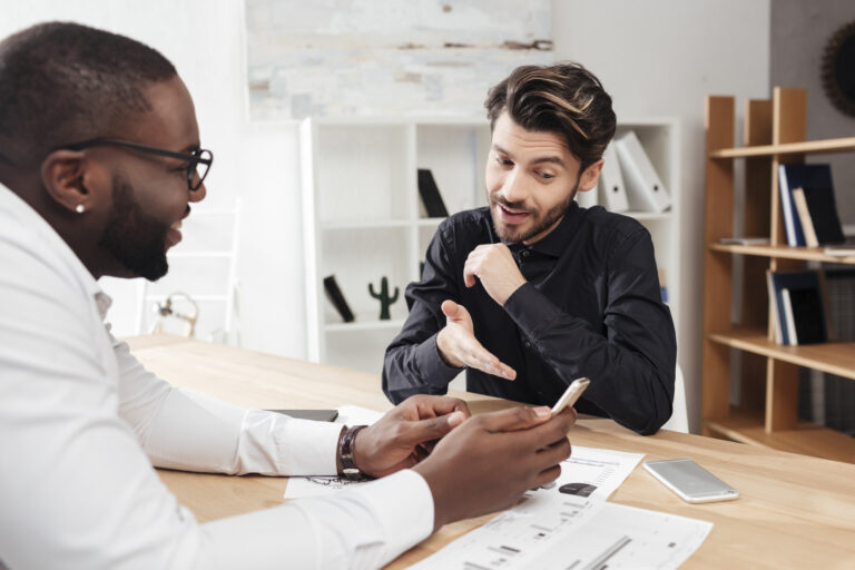 Two men sit at a table looking over charts and graphs.